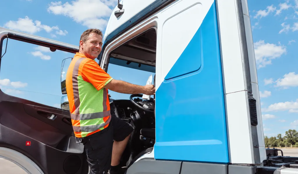 LKW-Fahrer in Warnweste steigt in das Fahrerhaus eines LKW