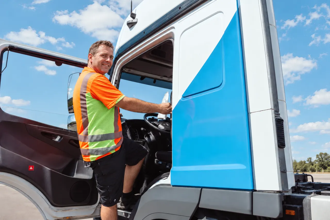 LKW-Fahrer in Warnweste steigt in das Fahrerhaus seines Sattelzugs