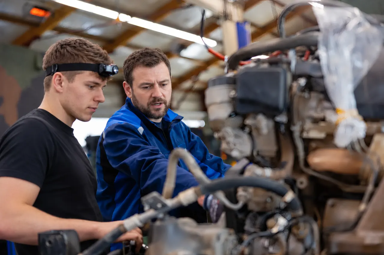 Zwei Mechaniker prüfen gemeinsam einen ausgebauten Fahrzeugmotor in der Werkstatt